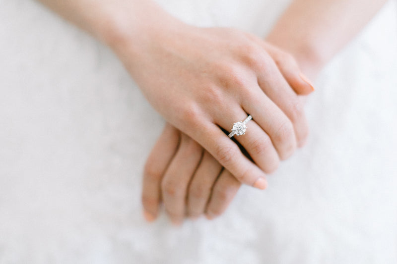 Close up photo of brides clasped hands in front of wedding dress with diamond engagement ring